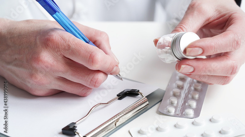 Close-up of a doctor hands writing a prescription in a medical record on a tablet. A doctor in a white coat holds pills in his hands and writes a prescription with a blue pen. Medical banner concept.