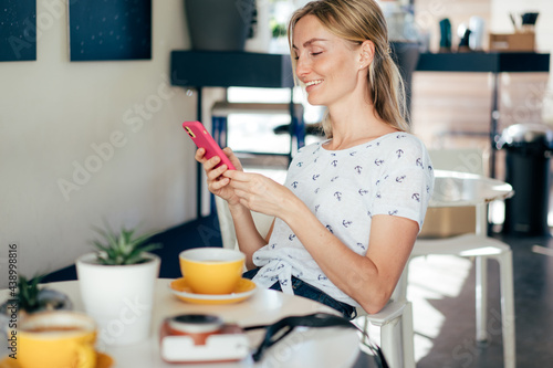 Young attractive woman sitting in the interior of a cafe chatting on the Internet on the phone. Woman uses mobile wireless technology for social networking
