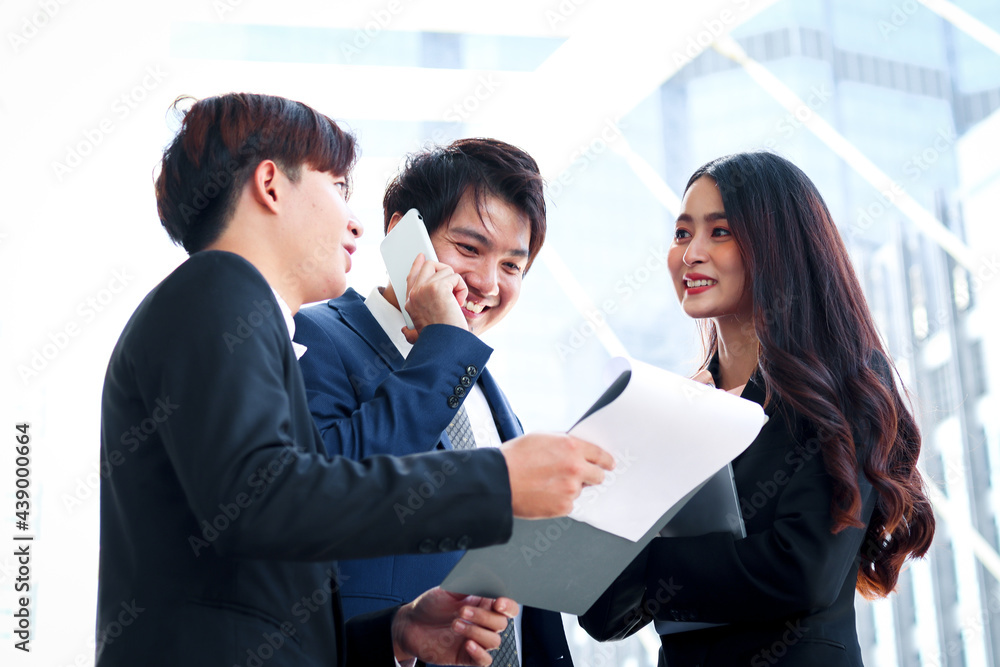 Group of three young Asian businesspeople socializing at modern city downtown with skyscraper building as blurred background., businessman and woman have meeting at outside office. Group of three young Asian businesspeople socializing at modern city downtown with skyscraper building as blurred background., businessman and woman have meeting at outside office.