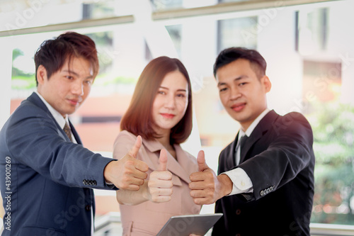 Group of three Asian businessman and woman confidential standing and giving thumbs up to camera, businesswoman holding digital tablet, businesspeople in downtown city.