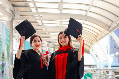 Two happy smiling graduated students, young beautiful Asian women celebrating successful education celebrating by throwing square academic hat cap on graduation day (commencement day) when have finish