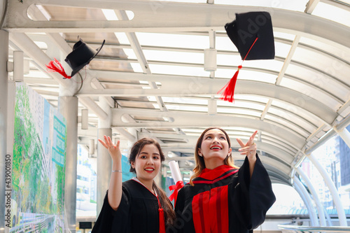 Two happy smiling graduated students, young beautiful Asian women celebrating successful education celebrating by throwing square academic hat cap on graduation day (commencement day) when have finish