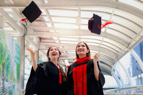 Two happy smiling graduated students, young beautiful Asian women celebrating successful education celebrating by throwing square academic hat cap on graduation day (commencement day) when have finish