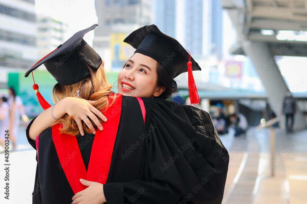 Two happy graduated women students with square academic hat cap hugging