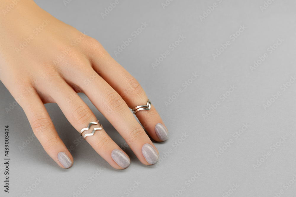 Beautiful groomed womans hand with minimal nail design on gray background Beautiful groomed womans hand with minimal nail design on gray background