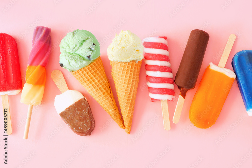 Variety of colorful summer popsicles and ice cream treats. Overhead view scattered on a pink background.