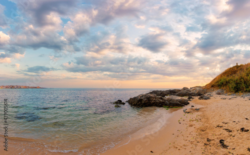 summer vacation landscape by the sea at sunrise. calm water washes sandy beach. dramatic clouds above horizon in morning light on the sky