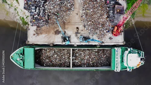 Cranes working simultaneously to load cargo ship with scrap metal at a tidal river port