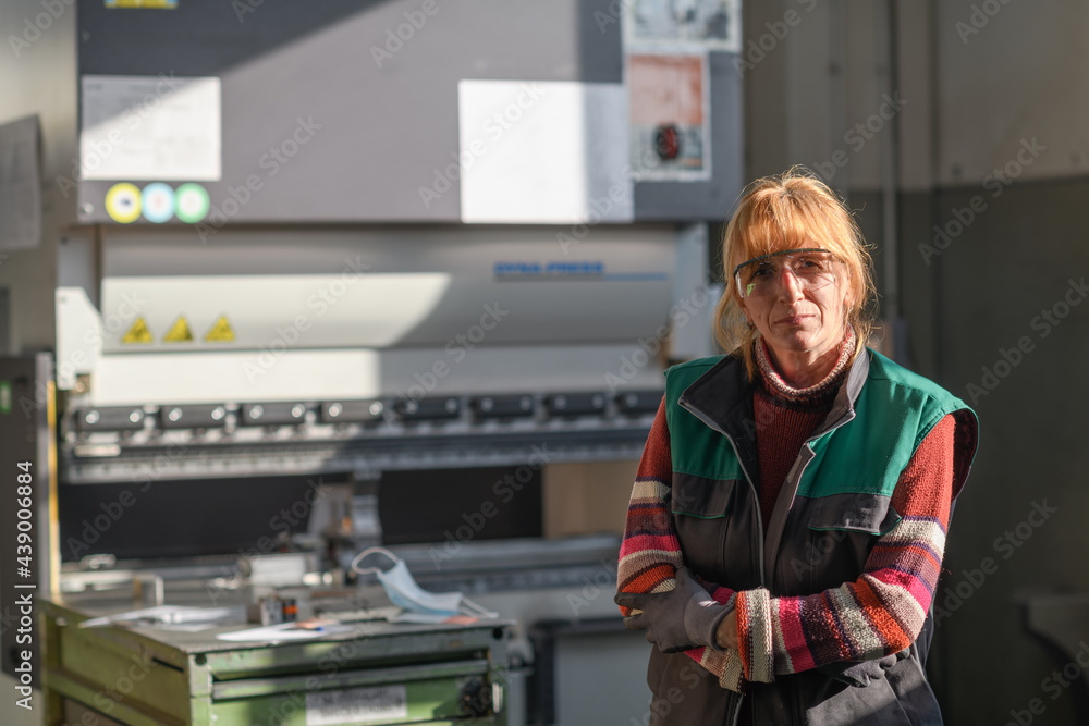 portrait of a woman standing in front of a CNC machine in goggles and working in a modern metal production and processing factory portrait of a woman standing in front of a CNC machine in goggles and working in a modern metal production and processing factory