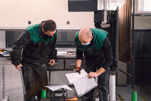 two workers wearing a protective mask due to a coronavirus pandemic, working in a modern factory and preparing a program and material for a cnc machine