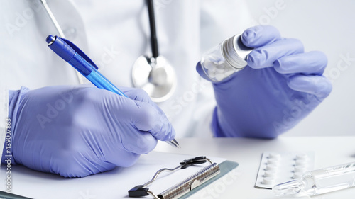 Close-up of doctor hands writing prescription in medical record on tablet.Doctor in white coat and blue gloves holds pills in his hands and writes prescription with blue pen.Medical banner concept.