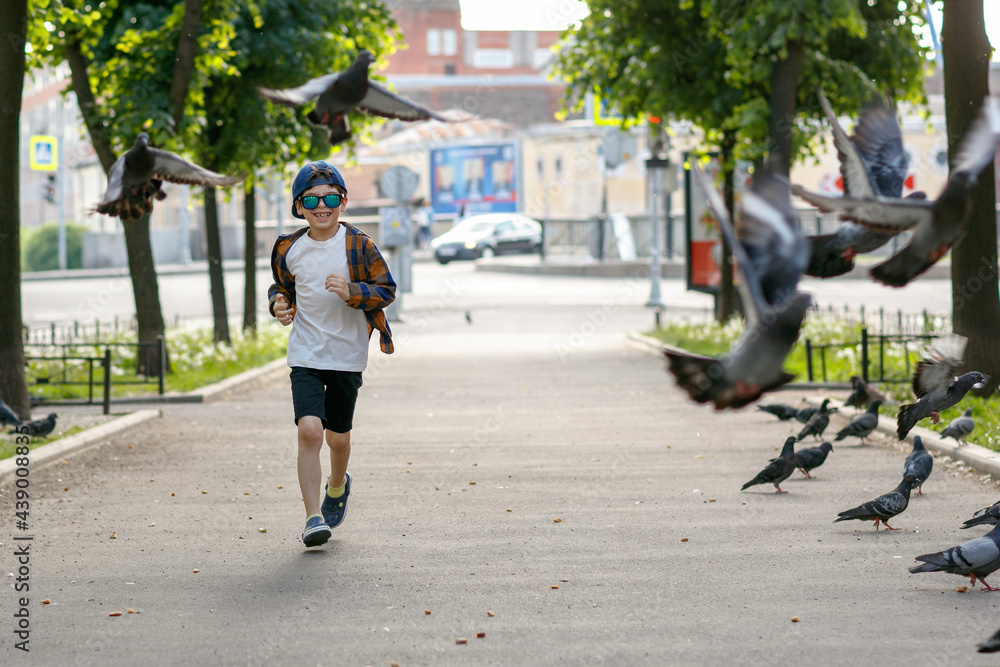 Fototapeta premium Boy playing with pigeons. A child in sunglasses on a walk