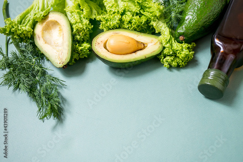 Green vegetables with glass boutle of oil on a green background. Avocado, Romano salad, greens. Top view. No plastic. Healthy diet concept