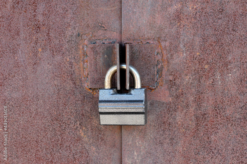 Old rusty metal door with corrosion and defects closed with a metal lock Old rusty metal door with corrosion and defects closed with a metal lock