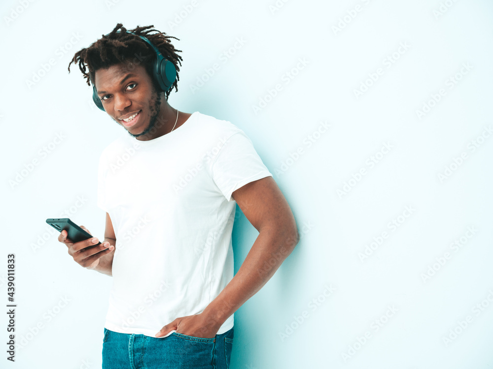 Handsome smiling hipster lambersexual model.Unshaven African man dressed in stylish clothes.Fashion male with dreadlocks hairstyle posing near wall in studio.Listening music in wireless headphones Handsome smiling hipster lambersexual model.Unshaven African man dressed in stylish clothes.Fashion male with dreadlocks hairstyle posing near wall in studio.Listening music in wireless headphones