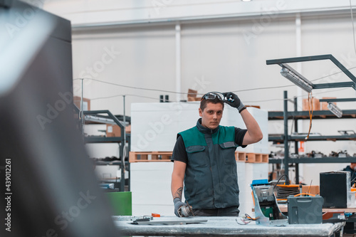 Heavy Industry Engineering Factory Interior with Industrial Worker Using Angle Grinder and Cutting a Metal Tube. Contractor in Safety Uniform and Hard Hat Manufacturing Metal Structures.