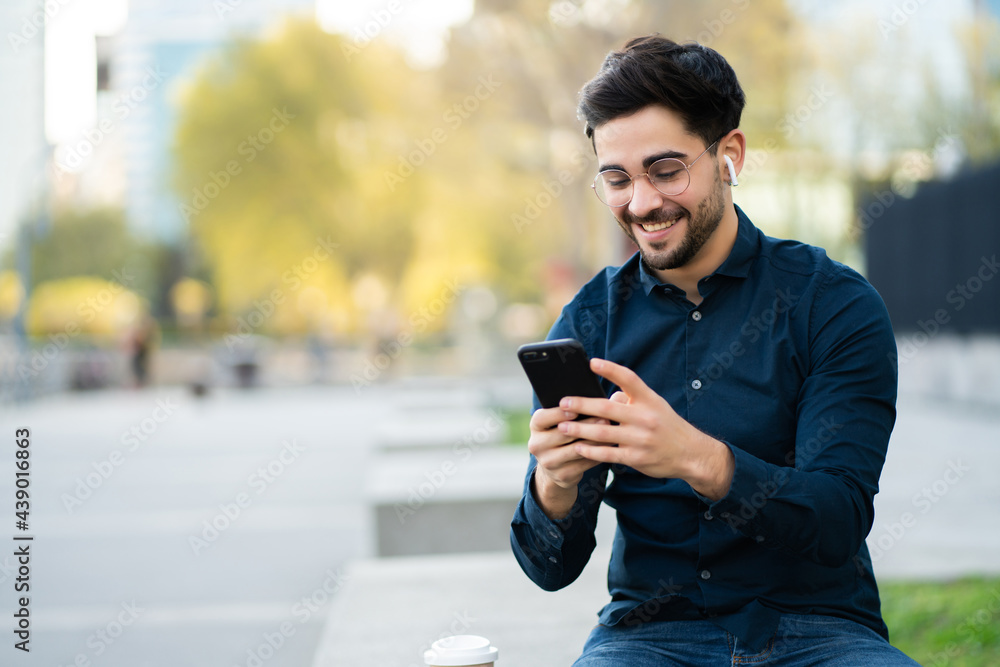 Young man using his mobile phone outdoors. - obrazy, fototapety, plakaty 
