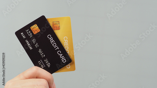 Hand is holding two credit card in black and gold color isolated on grey background.