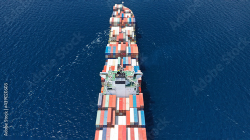 Aerial drone top down photo of industrial colourful vessel carrying heavy truck size containers cruising the Mediterranean deep blue sea