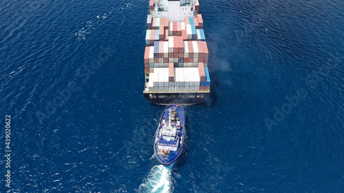 Aerial drone photo of tow - tug boat assisting by pulling or pushing container ship to anchor in terminal port photo