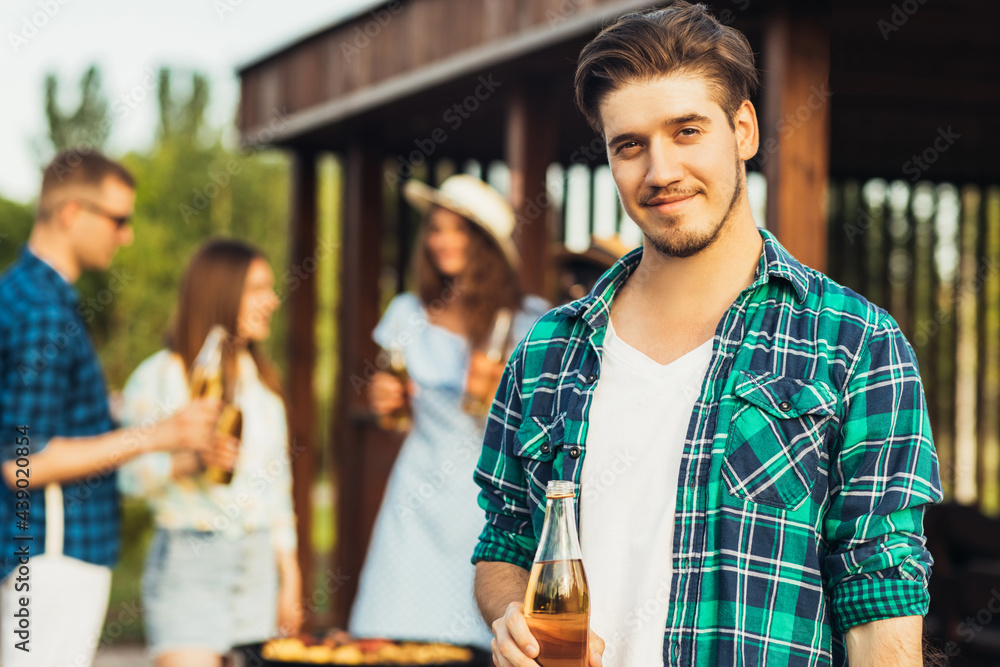 Young happy man in sunglasses having a group of friends having a barbecue with beer drinks having a rest in nature Young happy man in sunglasses having a group of friends having a barbecue with beer drinks having a rest in nature