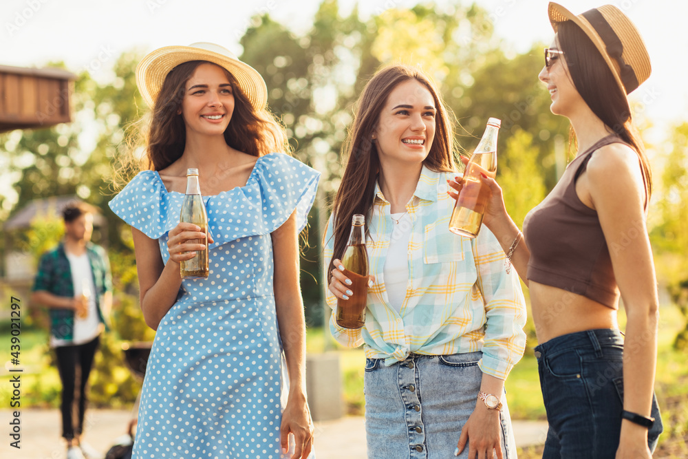 Three beautiful girlfriends having fun on a picnic, drinking drinks and chatting, a group of young friends doing barbecue on the grill Three beautiful girlfriends having fun on a picnic, drinking drinks and chatting, a group of young friends doing barbecue on the grill