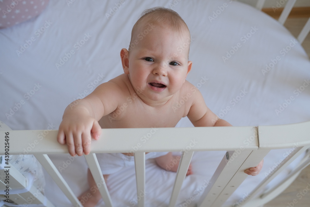 Close-up of a small child standing in a crib. The toddler does not want to sleep in the bed. Close-up of a small child standing in a crib. The toddler does not want to sleep in the bed.