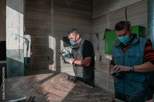 Industrial work during a pandemic. Two men work in a heavy metal factory, wearing a mask on their face due to a coronavirus pandemic