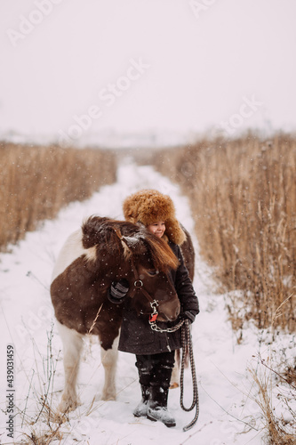 A two-colored pony and a child walk through a snow field 3093.