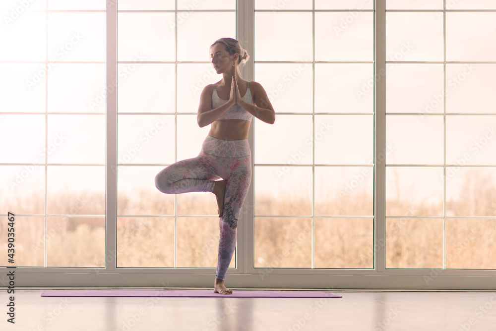Fototapeta premium Young attractive smiling woman practicing yoga, working out, wearing sportswear, bra, home