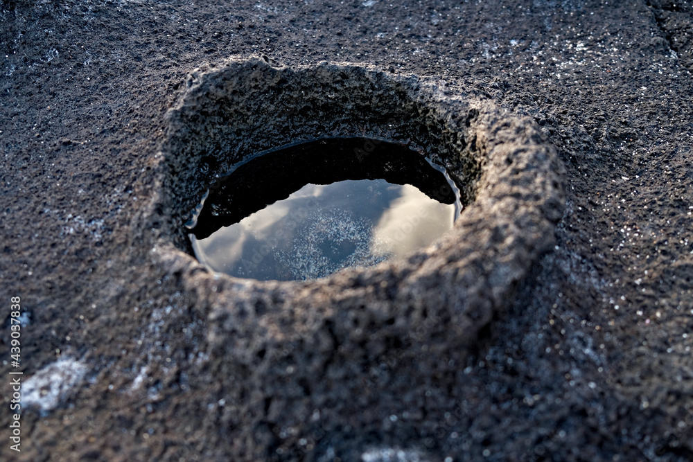 Micro crater with clean and clear water, sky and clouds reflected in the water, black basalt rock base in background. Micro crater with clean and clear water, sky and clouds reflected in the water, black basalt rock base in background.
