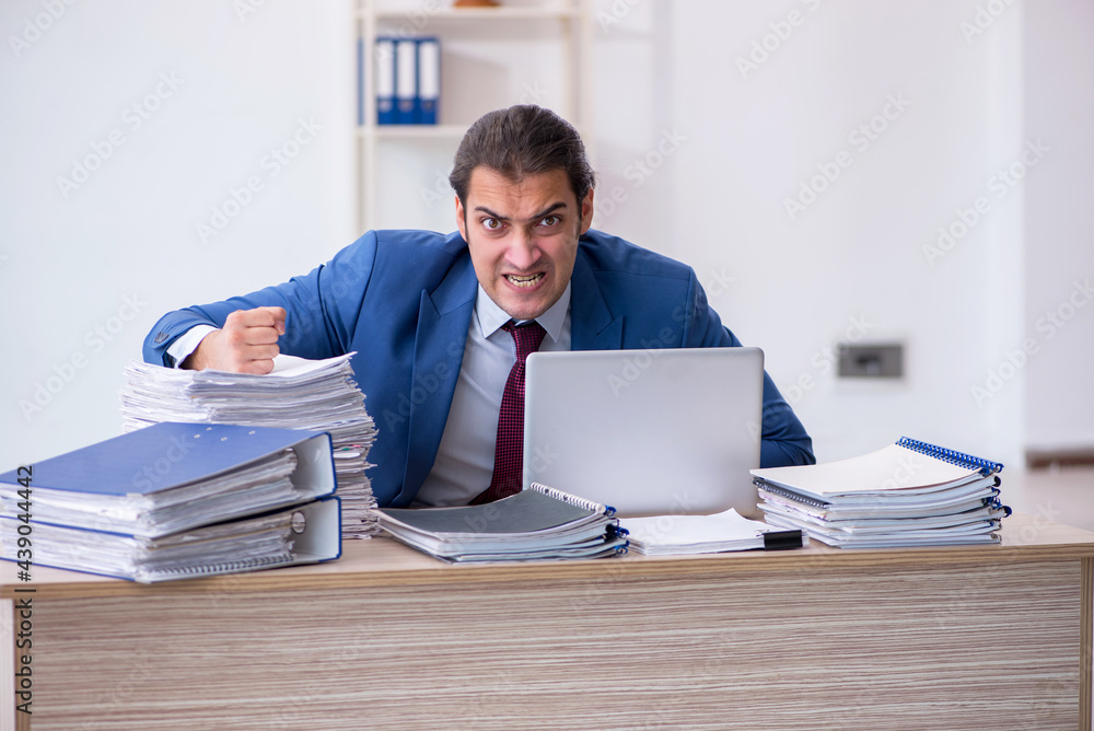 Young male employee unhappy with excessive work in the office Young male employee unhappy with excessive work in the office