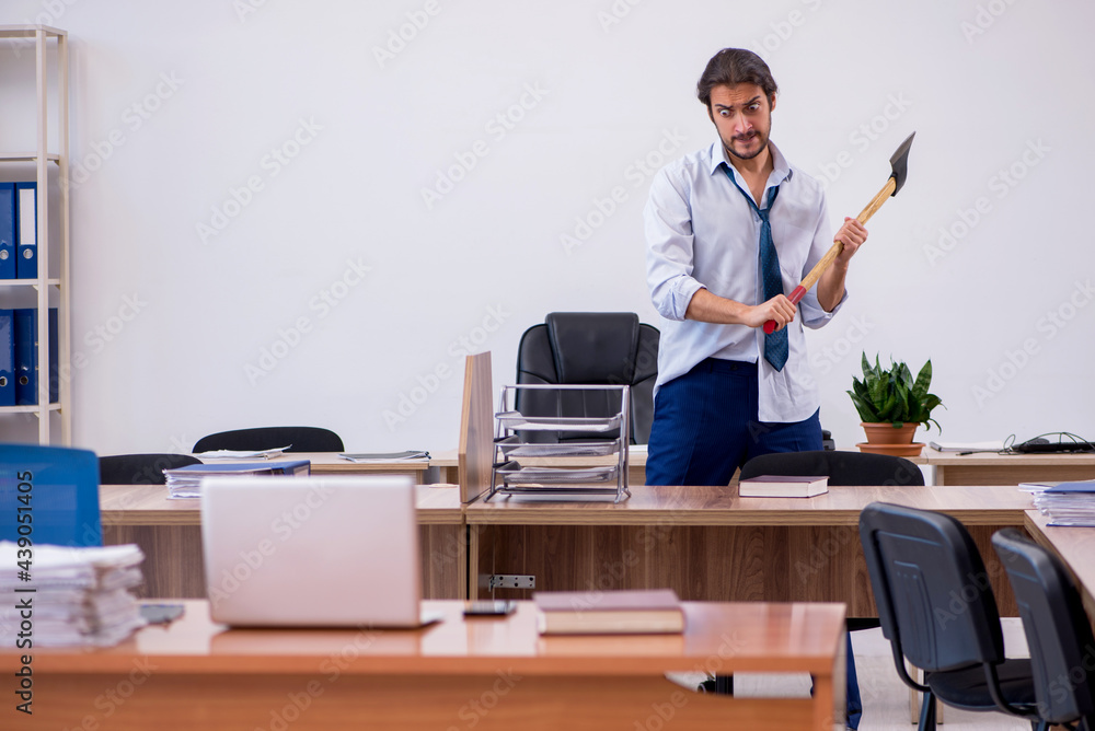 Young male furious employee holding hatchet in the office