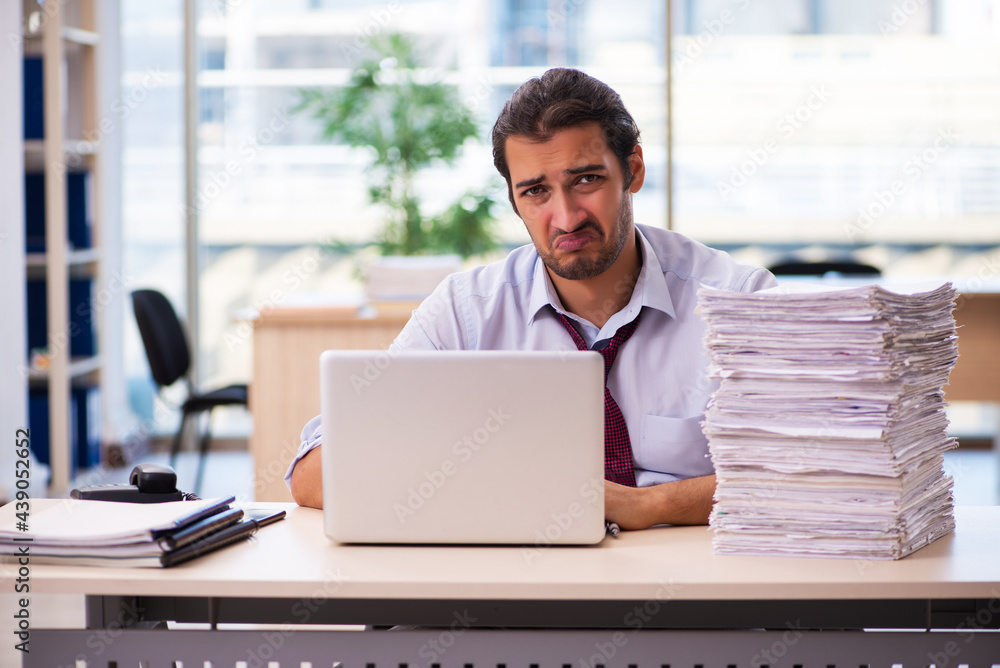 Young male employee unhappy with excessive work in the office Young male employee unhappy with excessive work in the office