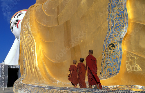 Myanmar, Monyma, Mandalay Division, Novice monks praying under giant statue of reclining Buddha in Lay Kyune Sakkyar temple photo