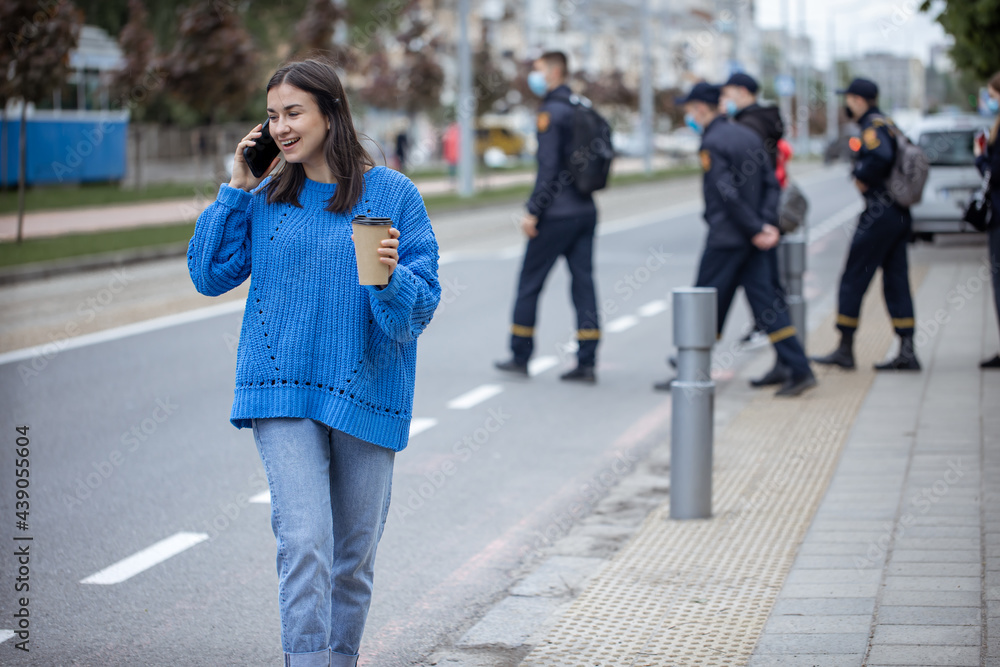 Stylish young girl speaks on the phone and holds coffee to go in her hand.
