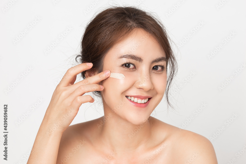 Happy young Asian woman with bare shoulders applying foundation cream on white background. Happy young Asian woman with bare shoulders applying foundation cream on white background.