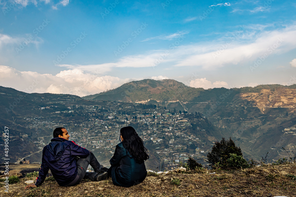 Fototapeta premium couple sitting at mountain top edge with crowded city structure and amazing sky at evening