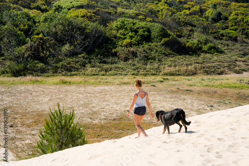 pretty young woman walking with her dog in the sand dunes photo