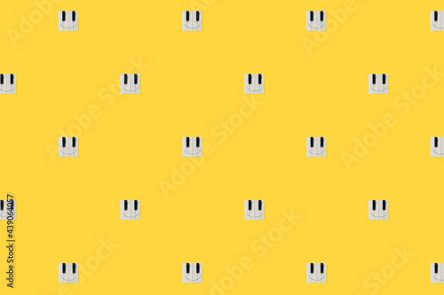 Creative, abstract happy face emoji icons texture with piano keys isolated on illuminating yellow background. Positive emotion music concept. Square emoticon pattern with copy space. Minimal flat lay.