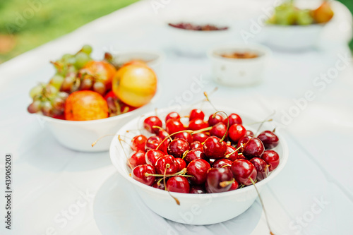 stylish food content. ripe cherry berry, ripe juicy apples, grapes and nuts in white paper plates on light table in an open space. healthy summer raw snacks for a party. selective fous photo