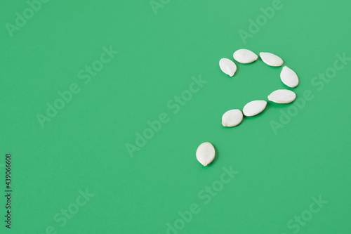 unpeeled pumpkin seeds laid out in the shape of a question mark on a green background