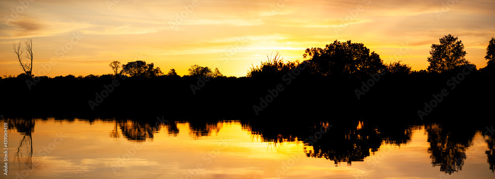 Sunset over the river, silhouette of the forest, mirror image in the water