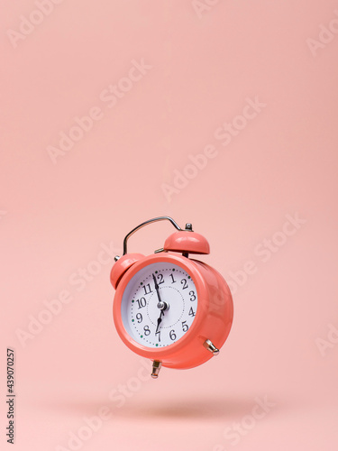 The pink alarm clock is levitate in the air, against a pink background. The concept of time, copy space.