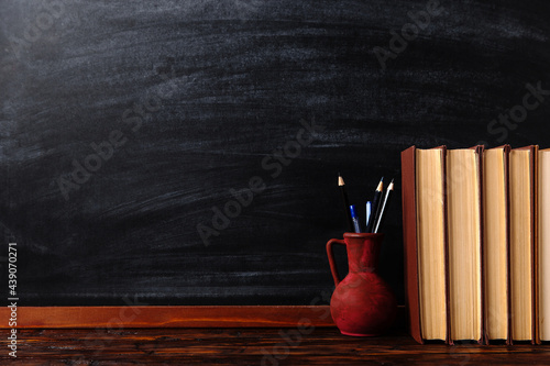 Books, pens and pencils in a jug on the table. Against the background of the chalkboard. Copy space.