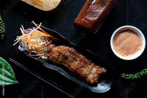 Sliced fried pork steak served with lettuce. Decorated with salad cream, peppers and other seasonings on a black tiled floor.