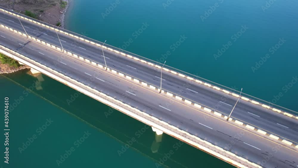 Top view of the empty bridge of the Kapchagai reservoir. The water is green. The bridge is reflected in the water. Birds fly. There are no cars. High poles with lighting. Kazakhstan, Almaty Top view of the empty bridge of the Kapchagai reservoir. The water is green. The bridge is reflected in the water. Birds fly. There are no cars. High poles with lighting. Kazakhstan, Almaty