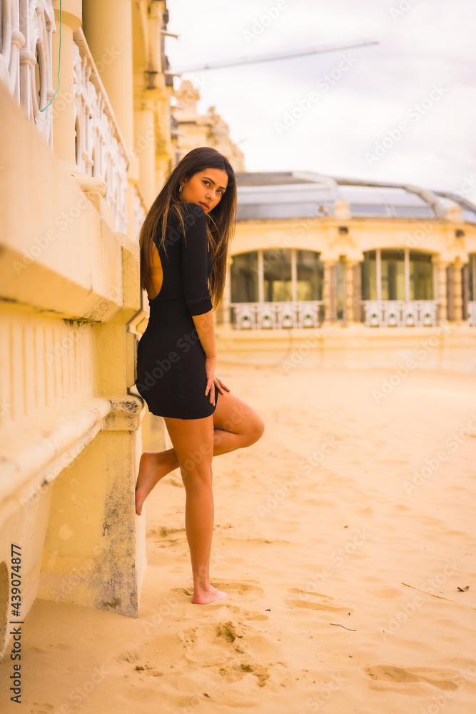 Lifestyle, portrait of a young brunette Caucasian woman in a short black dress on a beach enjoying the summer vacation