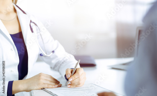 Unknown woman-doctor is prescribing some medication for her patient, using a clipboard, while sitting at the desk in her sunny cabinet. Female physician with a stethoscope, close up. Perfect medical