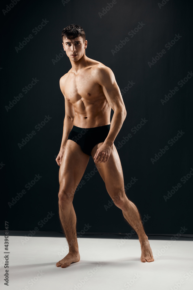 athletic men with a pumped-up muscular body in black shorts posing against a dark background